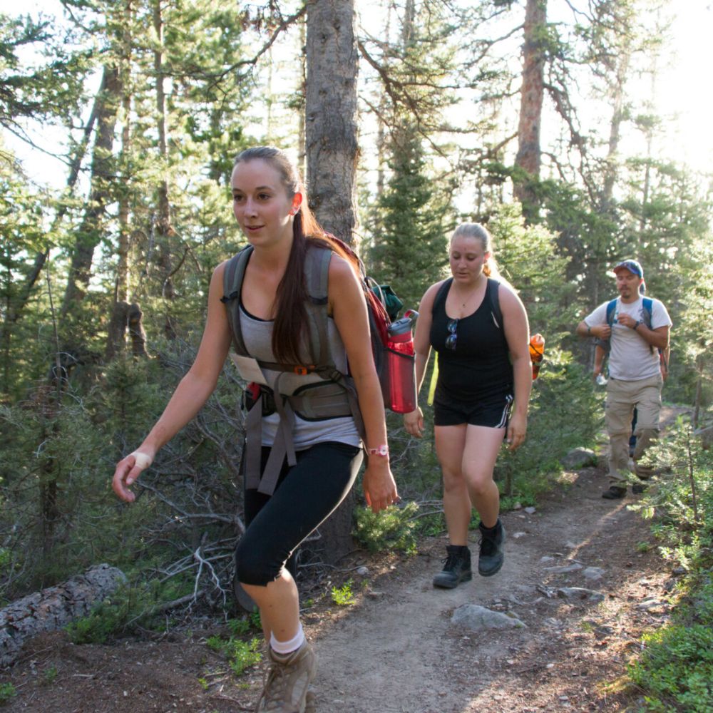 Two women hiking on a trail with backpacks in a forest