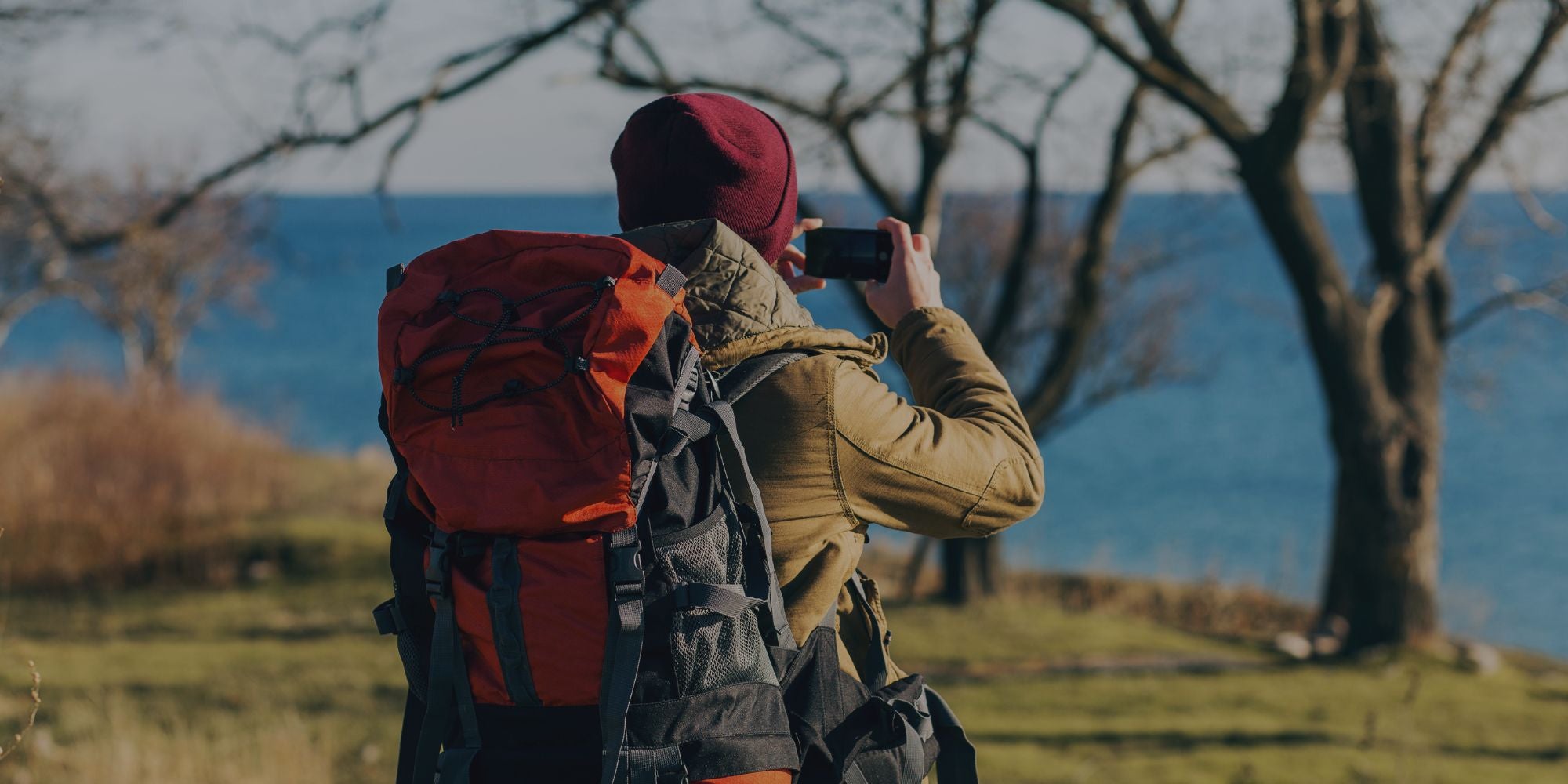 Person with a red backpack taking a photo by a body of water
